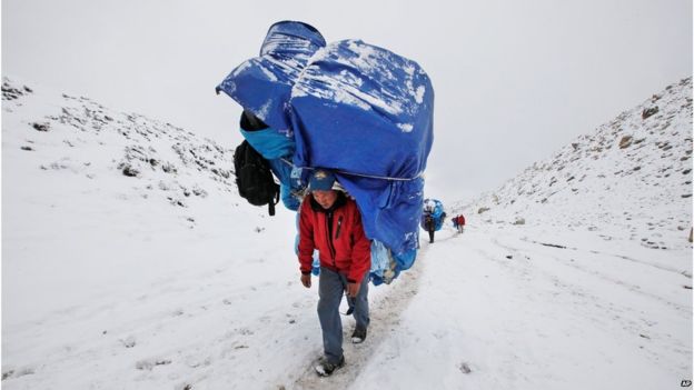 Ein Träger geht mit einer enormen Last in Richtung zu niedrigem Lager Everest